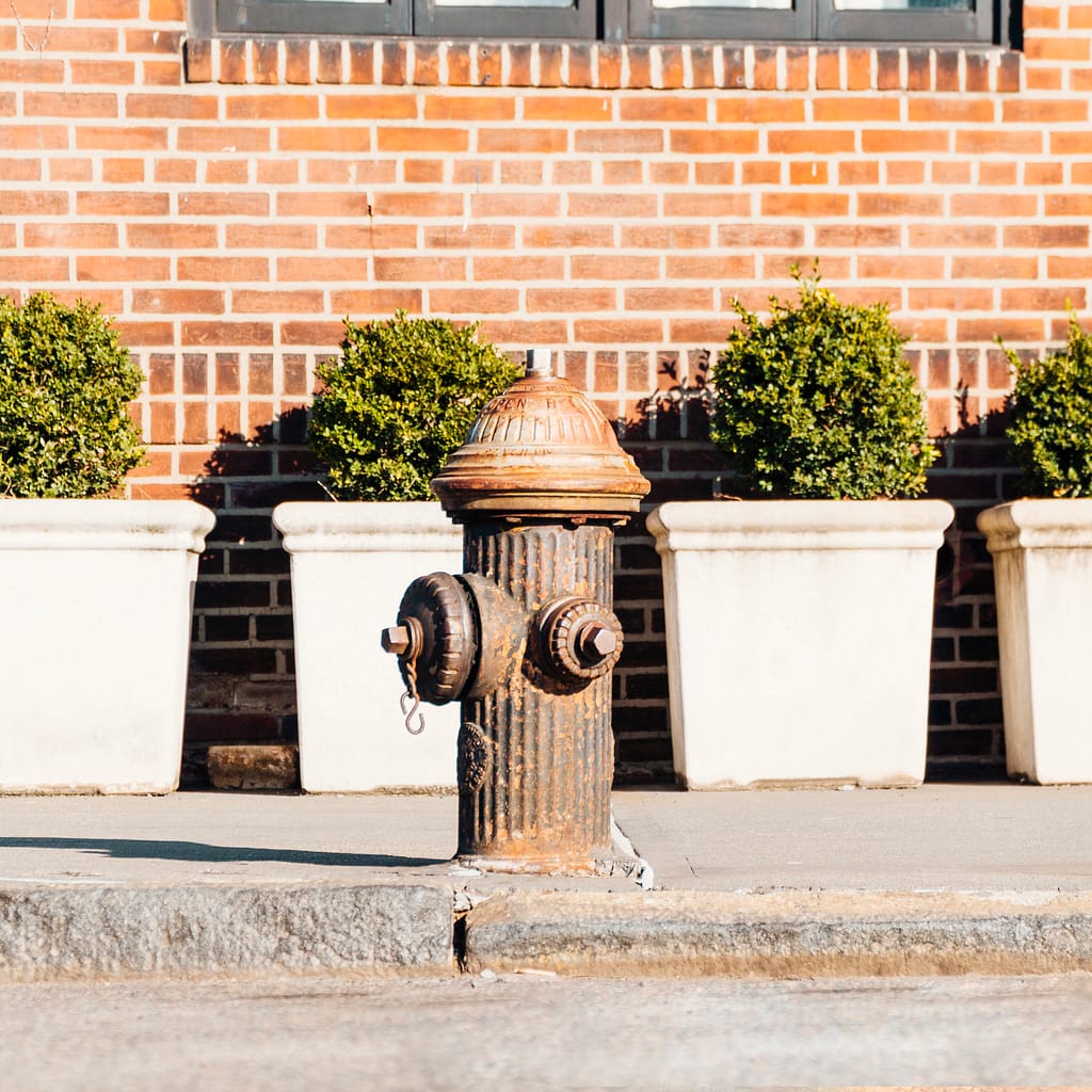 Weathered, yellow fire hydrant on a sidewalk beside a brick wall, showing signs of rust and age.
