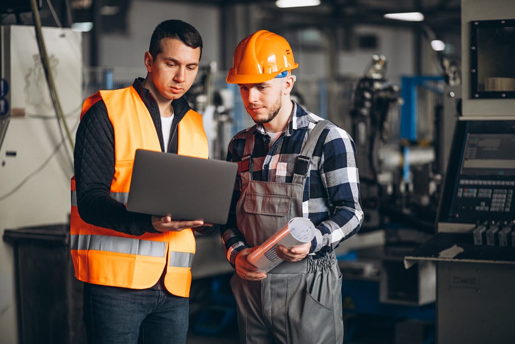Two workers in safety gear discussing or inspecting equipment in an industrial setting.