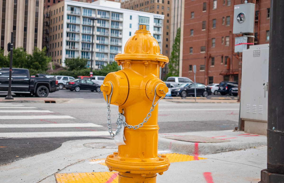 Bright yellow fire hydrant on a city sidewalk with buildings and parked cars in the background