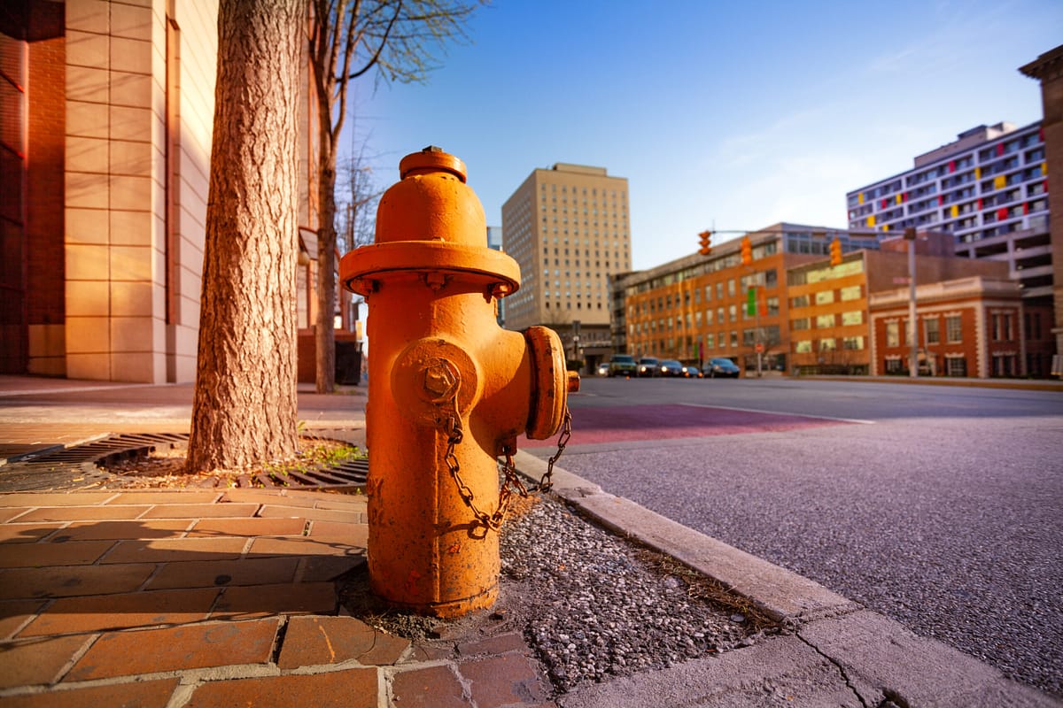 An orange fire hydrant on a brick-paved sidewalk in a quiet urban cityscape with buildings in the background.
