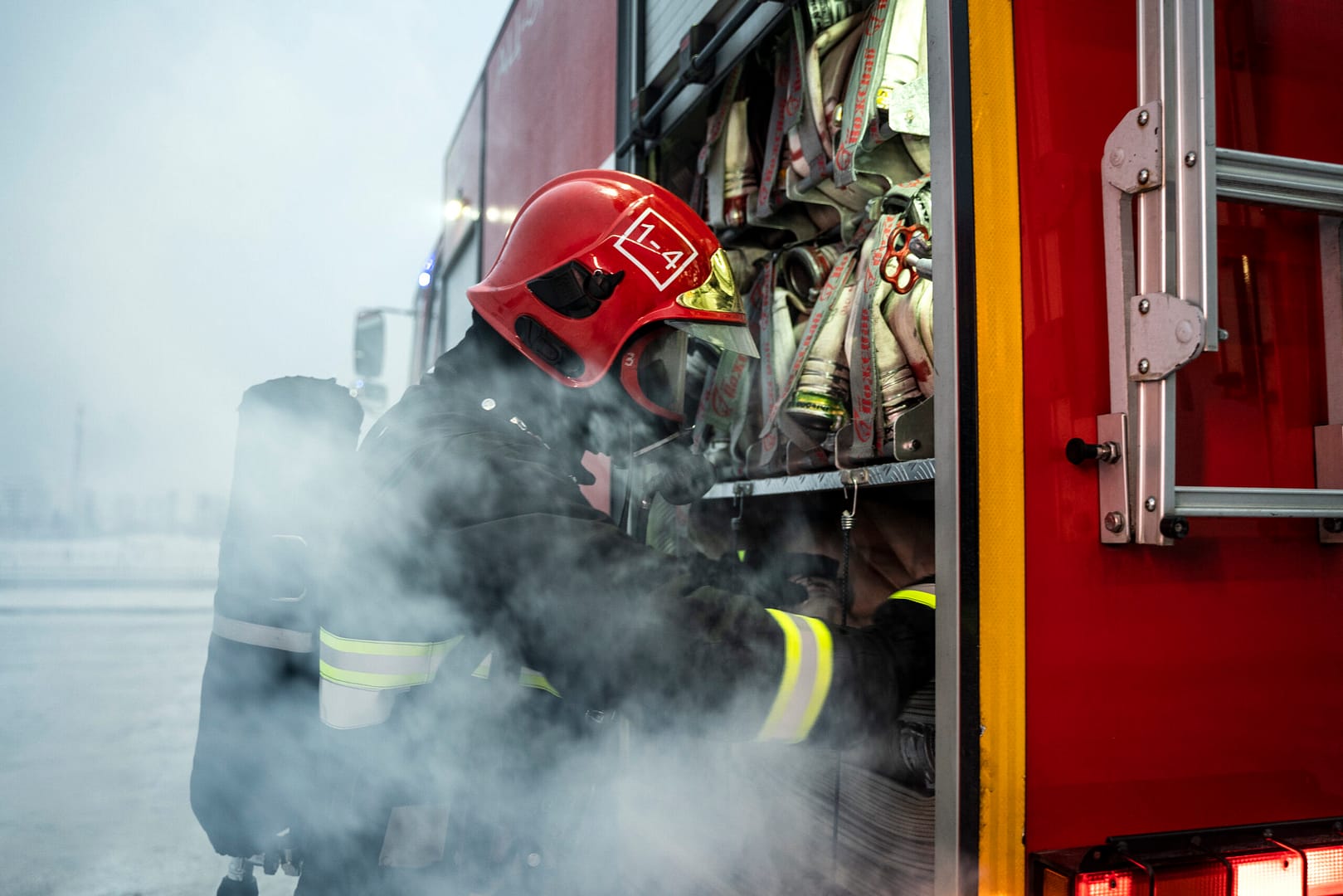 firefighter-ready-his-mission Male and female firefighters in full protective gear and helmets working together near a fire truck, appearing focused and cooperative during an emergency response. They understand where and how a blue fire hydrant is supposed to be used.
