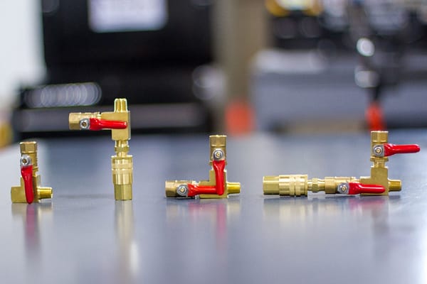 Brass fittings with red lever valves placed on a reflective surface