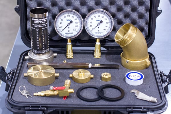 A toolkit containing flow accessories including gauges, brass fittings, hydrant flow nozzle chart, and other tools arranged inside a foam-lined case.